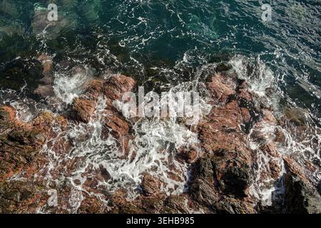 Blick aus der Vogelperspektive auf die felsige Küste mit Ozeanwellen und Meeresschaum bei sonnigem Wetter Stockfoto