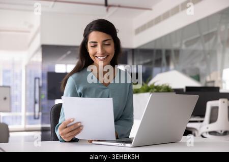 Lächelnde Geschäftsfrau liest Dokumente am Arbeitsplatz Stockfoto
