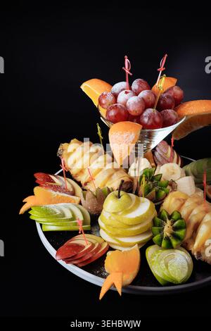 Luxuriöses Arrangement aus geschnitzten Äpfeln, Kiwi, Orangen und Trauben im Cocktailglas mit dekorativen Pflückern Stockfoto