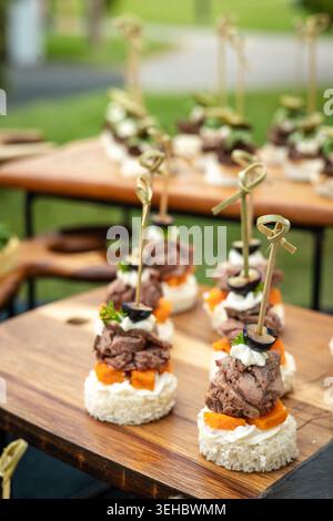 Elegante kleine Vorspeisen mit Fleisch und Oliven auf Holztabletts für ein Bankett. Stockfoto