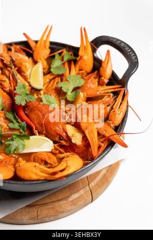 OP-Down Studio Shot zeigt einen Haufen leuchtend orange Krebse in einem schwarzen gusseisernen Topf mit Zitronenspalten und frischem Koriander isoliert auf Wi Stockfoto