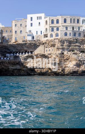 Polignano a Mare, Italien, Apulien - 24. Mai 2024: Gebäude auf Klippen gebaut, Blick vom Meer auf die Felsen und Höhlen von ​​picturesque.Terrasse mit weltberühmter Ruhe Stockfoto