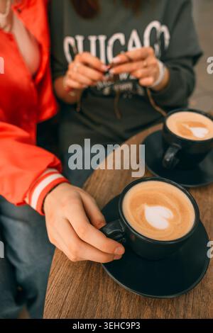Zwei Hände halten sich über einem Holztisch mit zwei Tassen Kaffee. Ein Notizbuch und dekorative Gegenstände befinden sich in einem gemütlichen Café Stockfoto