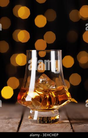 Whiskey-Glas mit bernsteinfarbener Flüssigkeit und Eis auf einem alten Holztisch Stockfoto