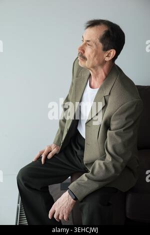 Kaukasischer Mann, Der Seitlich Sitzt, Hoffnungsvoller Blick Auf Das Fenster Und Leise Widerstandskraft Sichtbar In Der Haltung Ehemaliger Lehrer, Der Über Erinnerungen Nachdenkt Und Sich Umschließt Stockfoto