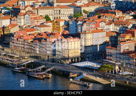 Erhöhter Blick auf das Ribeira-Ufer in Porto, Portugal, mit Booten auf dem Fluss Douro und sonnendurchfluteten historischen Häusern Stockfoto