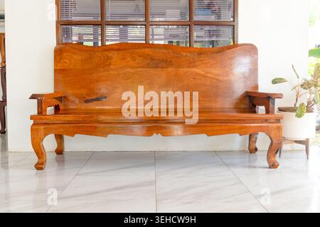 Lange braune Holzbank mit Armlehne wird den Gästen in der Lobby des Hotels oder Resorts serviert. Stockfoto