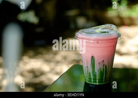 Erfrischender Eiskerne Matcha Latte mit Schichten rosafarbener Erdbeermilch und lebendigem grünem japanischem Uji Matcha-Grüntee-Sirup Stockfoto