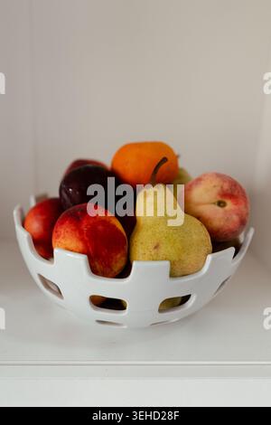 Farbenfrohe Vielfalt an frischem Obst, die eine dekorative Schüssel mit weißem Obst in einer hellen Umgebung füllt Stockfoto