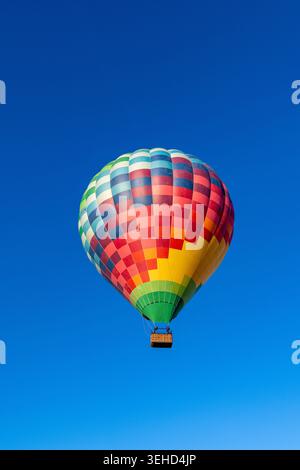 Ein farbenfroher Heißluftballon schwingt im blauen Himmel und zeigt ein lebendiges kariertes Muster. Passagiere genießen den Flug. Stockfoto