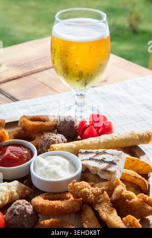 Bier- und Gemischter Snackteller, Verschiedene Käse, Nüsse, Oliven und herzhafte Vorspeisen, die zusammen für ein lockeres geselliges Beisammensein serviert werden Stockfoto