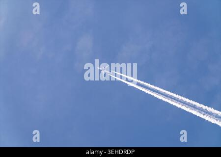 Passagierflugzeug, das in großer Höhe fliegt und weiße Kondensstreifen über dem klaren blauen Himmel hinterlässt. Minimale Luftfahrt-Szene, die Reisen, Bewegungen und Transpo symbolisiert Stockfoto
