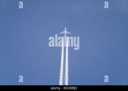 Passagierflugzeug, das in großer Höhe fliegt und weiße Kondensstreifen über dem klaren blauen Himmel hinterlässt. Minimale Luftfahrt-Szene, die Reisen, Bewegungen und Transpo symbolisiert Stockfoto