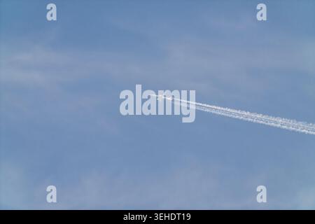 Passagierflugzeug, das in großer Höhe fliegt und weiße Kondensstreifen über dem klaren blauen Himmel hinterlässt. Minimale Luftfahrt-Szene, die Reisen, Bewegungen und Transpo symbolisiert Stockfoto