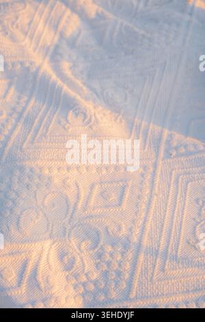 Sonnenlicht hebt Muster auf weißem Textil in den frühen Morgenstunden hervor. Sonnenlicht leuchtet und zeigt detaillierte Muster. Weiches Material fängt Licht ein. Stockfoto