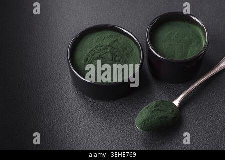 Lebensmittel, Gewürze, grüne Spirulina in Form von Pulver in einer schwarzen Schüssel auf dunklem Betonhintergrund Stockfoto