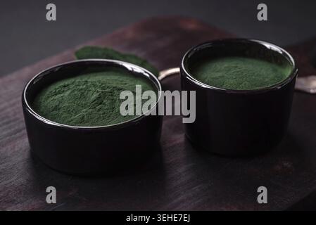 Lebensmittel, Gewürze, grüne Spirulina in Form von Pulver in einer schwarzen Schüssel auf dunklem Betonhintergrund Stockfoto