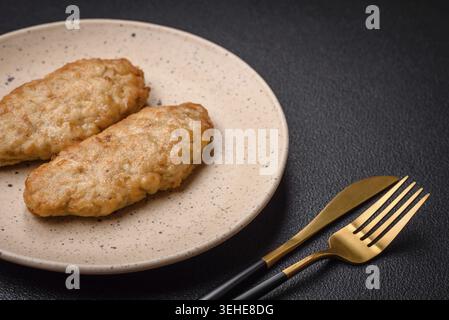 Essen, köstlicher frisch gebratener Hackfisch oder Hühnchenkoteletts mit Gewürzen und Kräutern auf dunklem Betonhintergrund Stockfoto