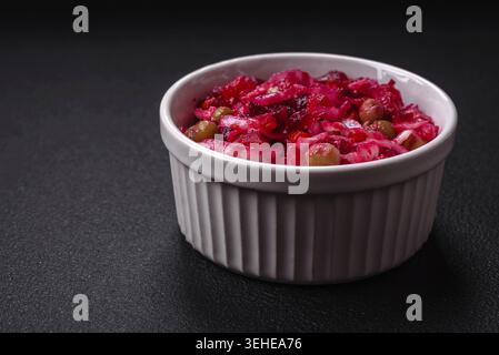Essen, köstlicher saftiger Vinigret Salat aus gekochtem Gemüse Kartoffeln, Rüben, Topf, Kohl und Karotten mit Salz und Gewürzen auf dunklem Betonhintergrund Stockfoto