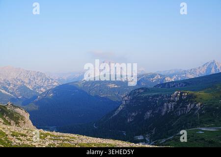 Weitläufige Berglandschaft mit mehrschichtigen Graten, felsigen Hängen und sanftem Morgenlicht, das weit entfernte Gipfel unter einem klaren blauen Himmel beleuchtet. Stockfoto