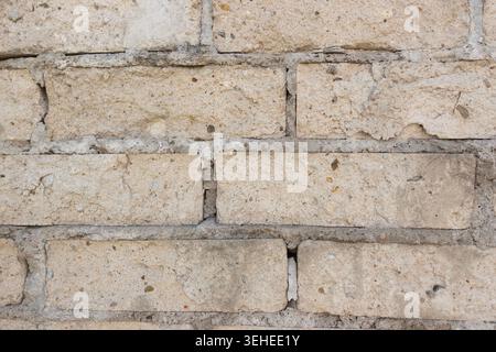 Nahaufnahme einer alten beigefarbenen Ziegelmauer mit gerissenem Mörtel, rauer Textur und verwittertem Mauerwerk Stockfoto