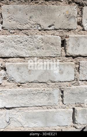 Nahaufnahme einer alten beigefarbenen Ziegelmauer mit gerissenem Mörtel, rauer Textur und verwittertem Mauerwerk Stockfoto