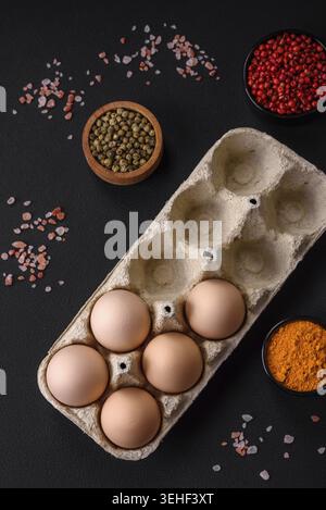 Essen, frische, rohe Hühnereier in beiger Farbe in einem Karton auf einem dunklen Betonhintergrund Stockfoto