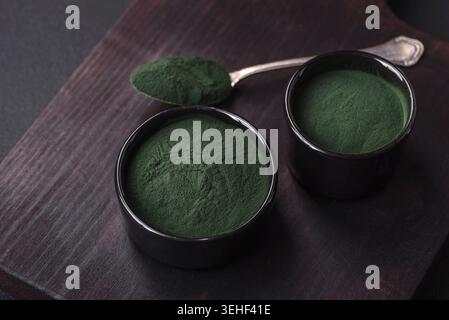 Lebensmittel, Gewürze, grüne Spirulina in Form von Pulver in einer schwarzen Schüssel auf dunklem Betonhintergrund Stockfoto