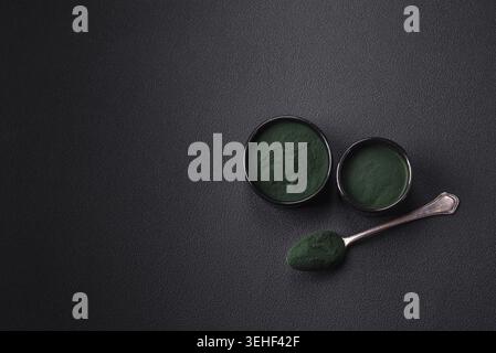 Lebensmittel, Gewürze, grüne Spirulina in Form von Pulver in einer schwarzen Schüssel auf dunklem Betonhintergrund Stockfoto