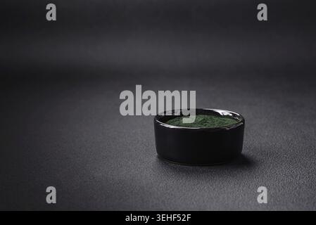 Lebensmittel, Gewürze, grüne Spirulina in Form von Pulver in einer schwarzen Schüssel auf dunklem Betonhintergrund Stockfoto
