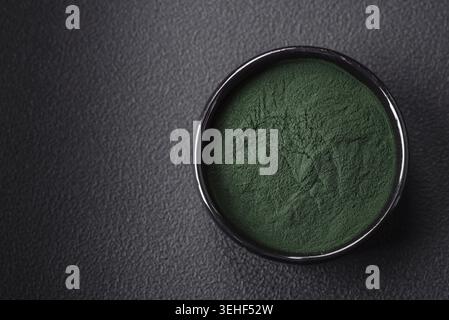 Lebensmittel, Gewürze, grüne Spirulina in Form von Pulver in einer schwarzen Schüssel auf dunklem Betonhintergrund Stockfoto