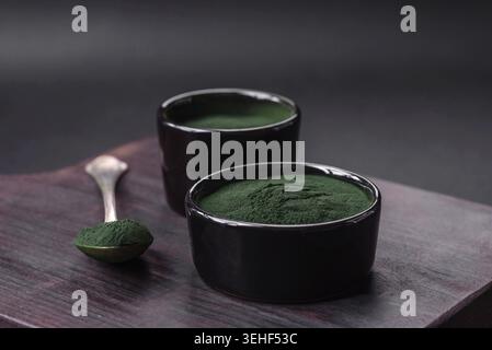 Lebensmittel, Gewürze, grüne Spirulina in Form von Pulver in einer schwarzen Schüssel auf dunklem Betonhintergrund Stockfoto
