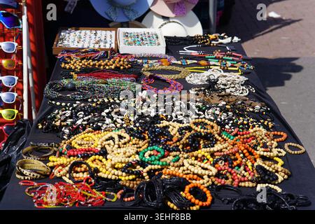 Farbenfroher Schmuckmarkt mit handgefertigten Perlen-Halsketten, Armbändern, Holzperlen und Sonnenbrillen an einem sonnigen Tag in Brighton, England. Stockfoto
