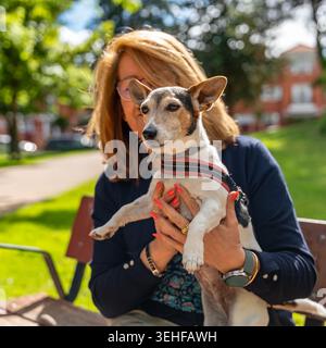 Frau mit einem kleinen Jack Russell Hund, der auf einer Parkbank sitzt Stockfoto