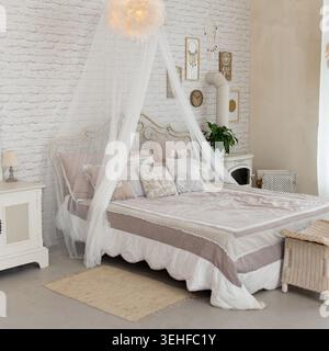 Gemütliches Schlafzimmer in Boho Shabby Chic Stil. Mit Himmelbett, weißer Ziegelwand und Vintage-Möbeln. Weiche, neutrale Farben wie beige und cremefarbene Crea Stockfoto