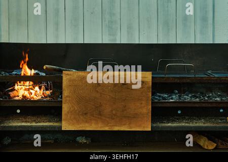 Holzscheite brennen in einem rustikalen Grill im Freien mit Holzkohle zum Kochen, ein hölzernes Schneidebrett daneben Stockfoto