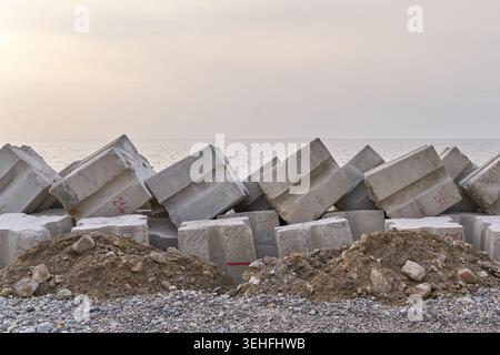 Betonblöcke, die einen Wellenbrecher an einem Kiesstrand bilden und Küstenerosion vor den Meereswellen schützen Stockfoto