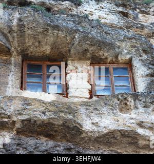 Zwei Holzfenster in einer felsigen Klippe. Die Steinstruktur ist rau und verwittert, was auf natürliche Erosion hinweist. Die Szene hebt das einzigartige Archit hervor Stockfoto