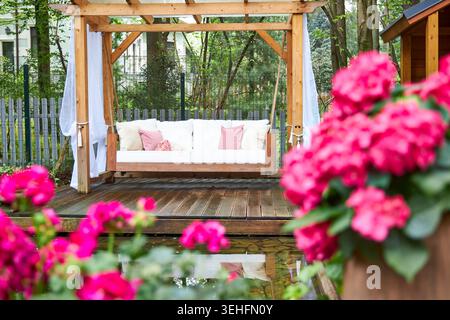 Elegante Pergola-Schaukel aus Holz mit blühenden rosa Hortensien in Garden Retreat Stockfoto