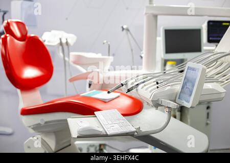 Moderner Zahnarztstuhl mit Behandlungsgeräten. Helle Einrichtung der Zahnklinik mit rotem Patientenstuhl, Behandlungswerkzeugen, digitalem Bildschirm und modern Stockfoto