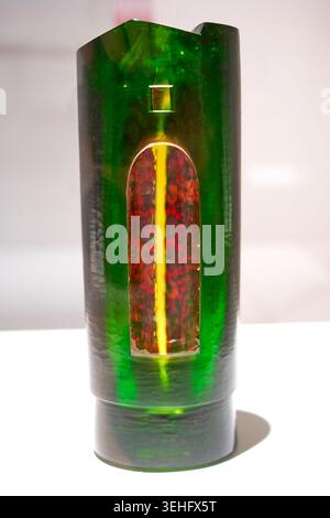 Eine große, zylindrische grüne Glasskulptur mit einer strukturierten Oberfläche steht vor einem schlichten weißen Hintergrund. Das Kunstwerk zeigt ein gewölbtes Fenster Stockfoto