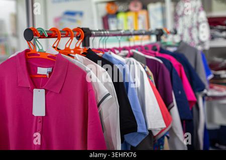 Bunte Poloshirts hängen im Store. Nahaufnahme farbenfroher Polohemden an Kleiderbügeln in einem Einzelhandelsgeschäft mit leerem Preisschild und weichem Hintergrund. Stockfoto