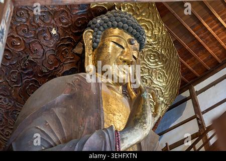 Nahaufnahme einer großen goldenen Buddha-Statue in einem traditionellen japanischen Tempel. Die Buddha-Figur zeigt einen gelassenen Ausdruck mit geschlossenen Augen, Stockfoto