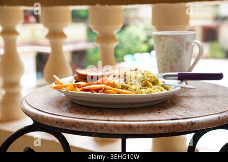 Frühstücksteller mit Kaffeetasse auf Balkontisch in sanftem Morgenlicht Stockfoto