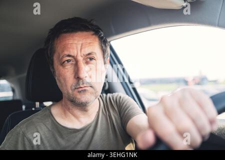 Mann mittleren Alters, der ein Auto mit einem konzentrierten, durchdachten Ausdruck fährt, während er tagsüber das Lenkrad greift oder unterwegs ist. Selektiv fo Stockfoto