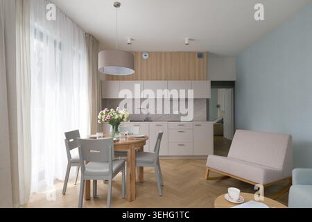 Das Innere eines hellen, modernen Studio-Apartments verfügt über eine kleine Küchenzeile mit Holztisch mit Stühlen und einen gemütlichen Wohnbereich mit Parkettboden Stockfoto