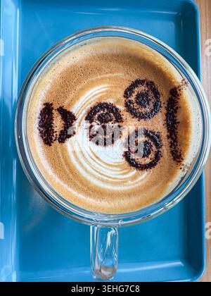 Tasse Kaffee mit dekorativem 100-Design auf dem Milchschaum, von oben auf einem hellblauen Tablett fotografiert. Stockfoto