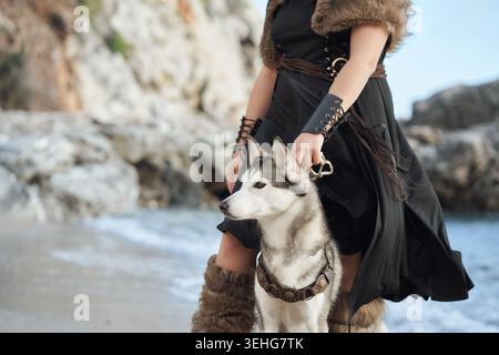 Eine Frau hält einen sibirischen Husky-Hund am Meer. Detaillierte Nahkomposition unterstreicht emotionale Verbindung und Outdoor-Lifestyle-Stimmung an der Küste Stockfoto