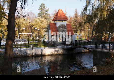 Eine malerische Parkszene mit einem Steingebäude mit einem roten Dach neben einem ruhigen Fluss. Bäume umgeben den Bereich und schaffen eine ruhige Atmosphäre Stockfoto