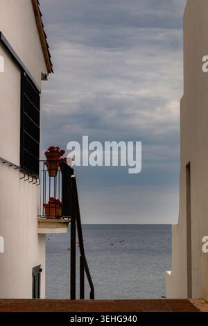Weiße architektonische Fassade mit roten Blumen auf einem Balkon mit Blick auf das Meer und Bojen Stockfoto